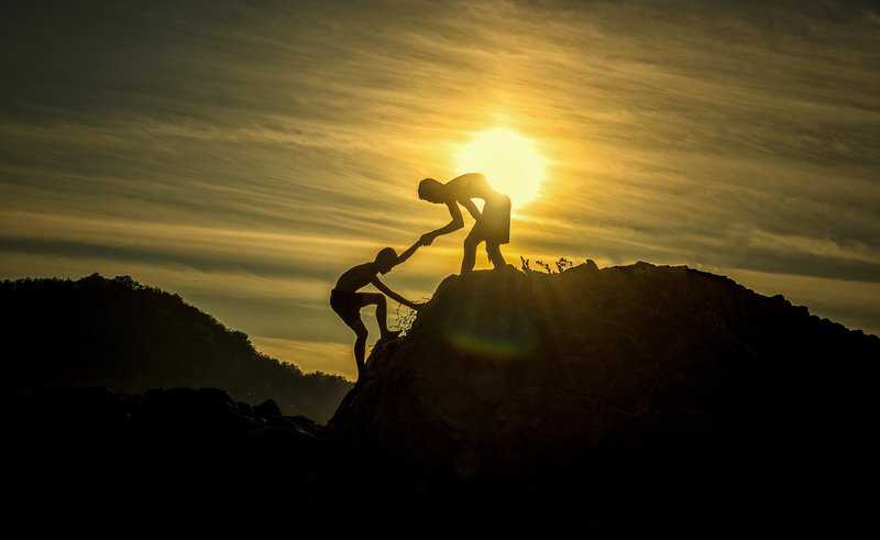 kid helping anothe kid climb mountain